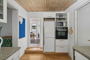 Eine kleine Küche mit Kühlschrank, Mikrowelle und Backofen, Holzboden und Blick auf einen Außenbereich.