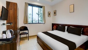 Ein Hotelzimmer mit Bett, Fernseher, Schreibtisch mit Wasserkocher, Stuhl und einem Fenster mit Vorhängen.
