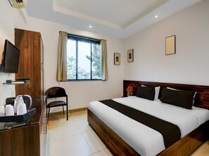 Ein Hotelzimmer mit Bett, Fernseher, Schreibtisch mit Wasserkocher, Stuhl und einem Fenster mit Vorhängen.