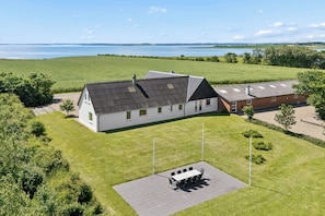 A house with a large lawn, a patio with a table and chairs, and a view of a lake. - Spacious holiday home with water view (Redsted)