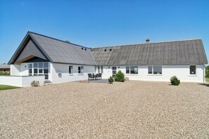 A modern building with a gravel driveway and a covered outdoor seating area. - Spacious holiday home with water view (Redsted)