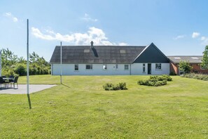 A building with a sloped roof, a flat front, and a small front yard with a lawn and bushes. - Spacious holiday home with water view (Redsted)