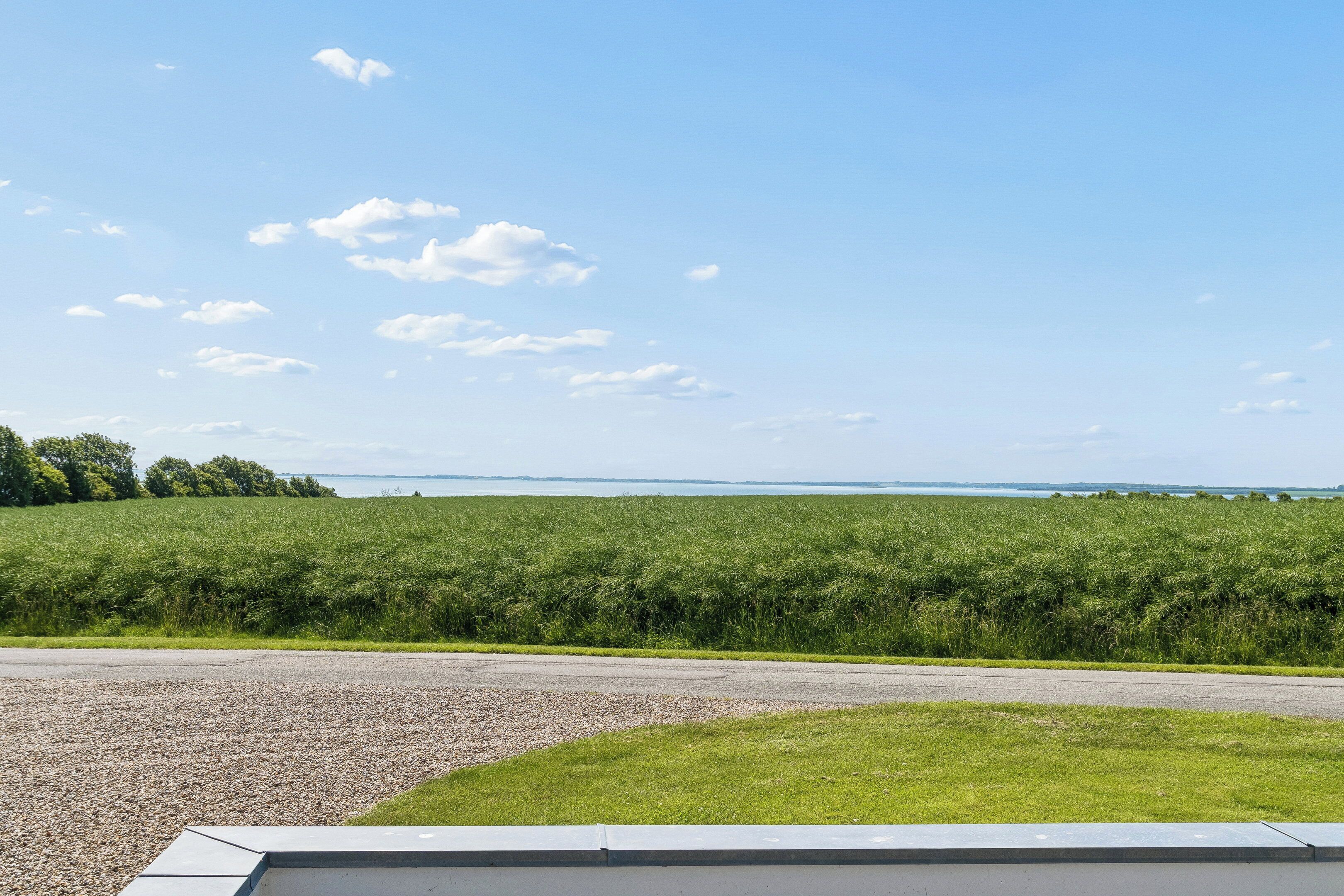 A clear sky, a gravel road, and a grassy field with a distant body of water.