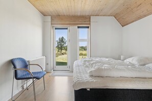 A bedroom with a bed, a chair, a radiator, and a view through a door. - Spacious holiday home with water view (Redsted)