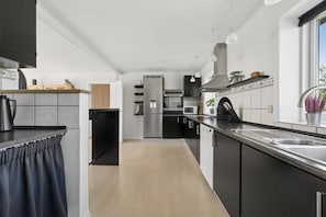 A modern kitchen with a central island, stainless steel appliances, and a window providing natural light. - Spacious holiday home with water view (Redsted)
