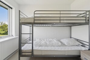 Ein Etagenbett mit Fenster, weißer Bettwäsche und einem Holfnachtkästchen.