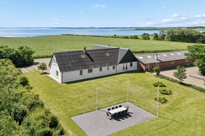 A house with a large lawn, a patio with a table and chairs, and a view of a lake. - Spacious holiday home with water view (Redsted)