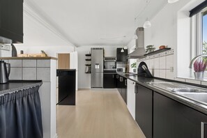 A modern kitchen with a central island, stainless steel appliances, and a window providing natural light. - Spacious holiday home with water view (Redsted)