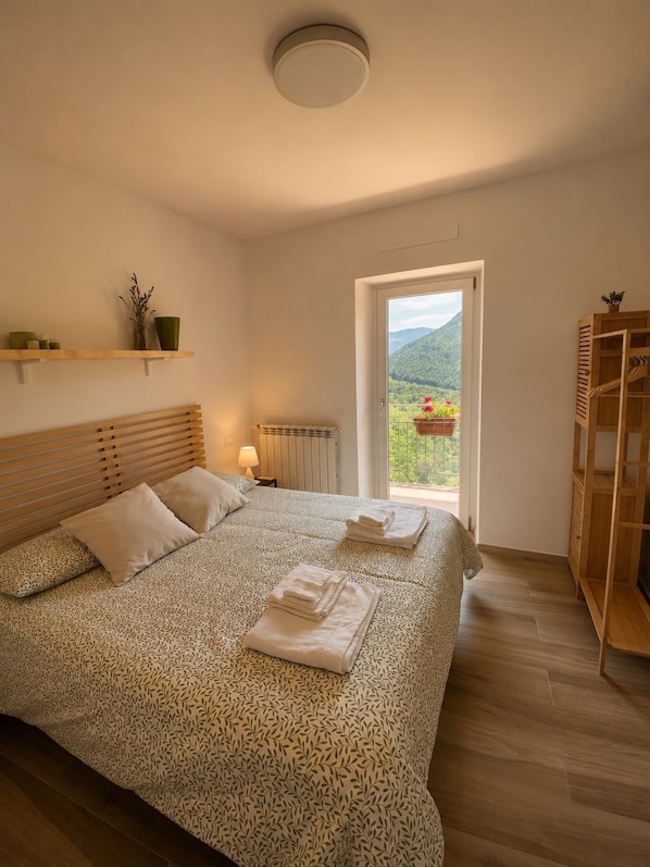 Ein Schlafzimmer mit einem Bett, einem Heizkörper, einem Fenster mit Blick und einer Holzablage.