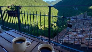 A balcony with two coffee cups, a metal railing, and a view of green hills and a river.