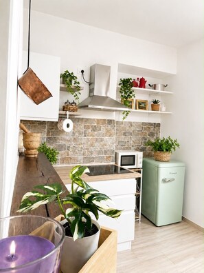 Een moderne keuken met een betegelde achterwand, witte kastjes, een magnetron, een vintage koelkast en potplanten.