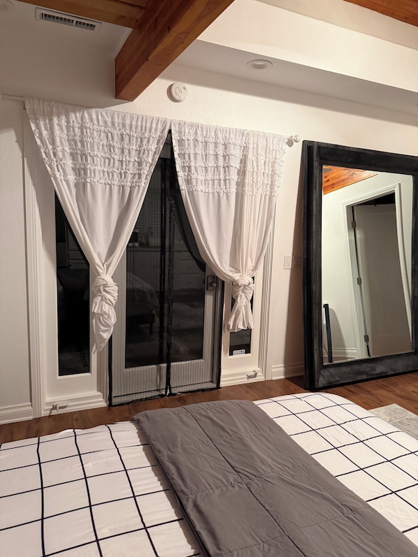 A room with a large mirror, a sliding glass door with white curtains, and a patterned rug.