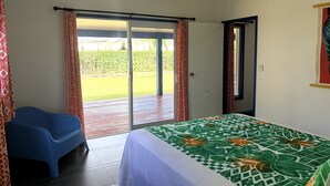 A bedroom with a bed, a blue chair, and a sliding glass door to a patio. - Kuki Kainga (Matavera District)