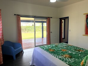Un dormitorio con cama, una silla azul y puerta corrediza de vidrio a un patio.