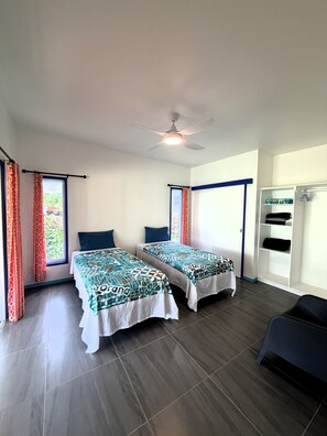 A room with two beds, a ceiling fan, a window with curtains, a wardrobe, and a chair. - Kuki Kainga (Matavera District)