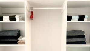 A white closet with shelves holding folded towels and a tropical-patterned pillow. - Kuki Kainga (Matavera District)