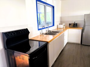 A modern kitchen with a black stove, stainless steel sink, and a microwave. - Kuki Kainga (Matavera District)