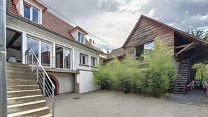 Ein zweistöckiges Haus mit einem Schotterweg, einer Holztreppe und einer kleinen Terrasse mit Gartenmöbeln.