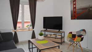 Ein modernes Wohnzimmer mit einer Couch, einem Fernseher, einem Bücherregal, einem einzigartigen Sessel und einem Gemälde der Golden Gate Bridge.