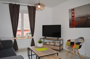 A modern living room with a sofa, a TV, a bookshelf, a unique chair, and a painting of the Golden Gate Bridge.