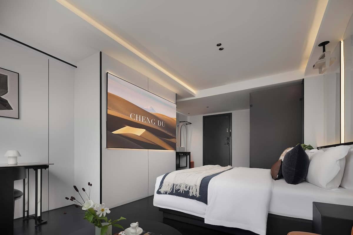 Une chambre d’hôtel moderne avec un grand lit, un bureau, un téléviseur fixé au mur et une porte de salle de bain.