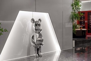 A metallic sculpture of a bear in a modern lobby with a reflective floor and a plant in the background.
