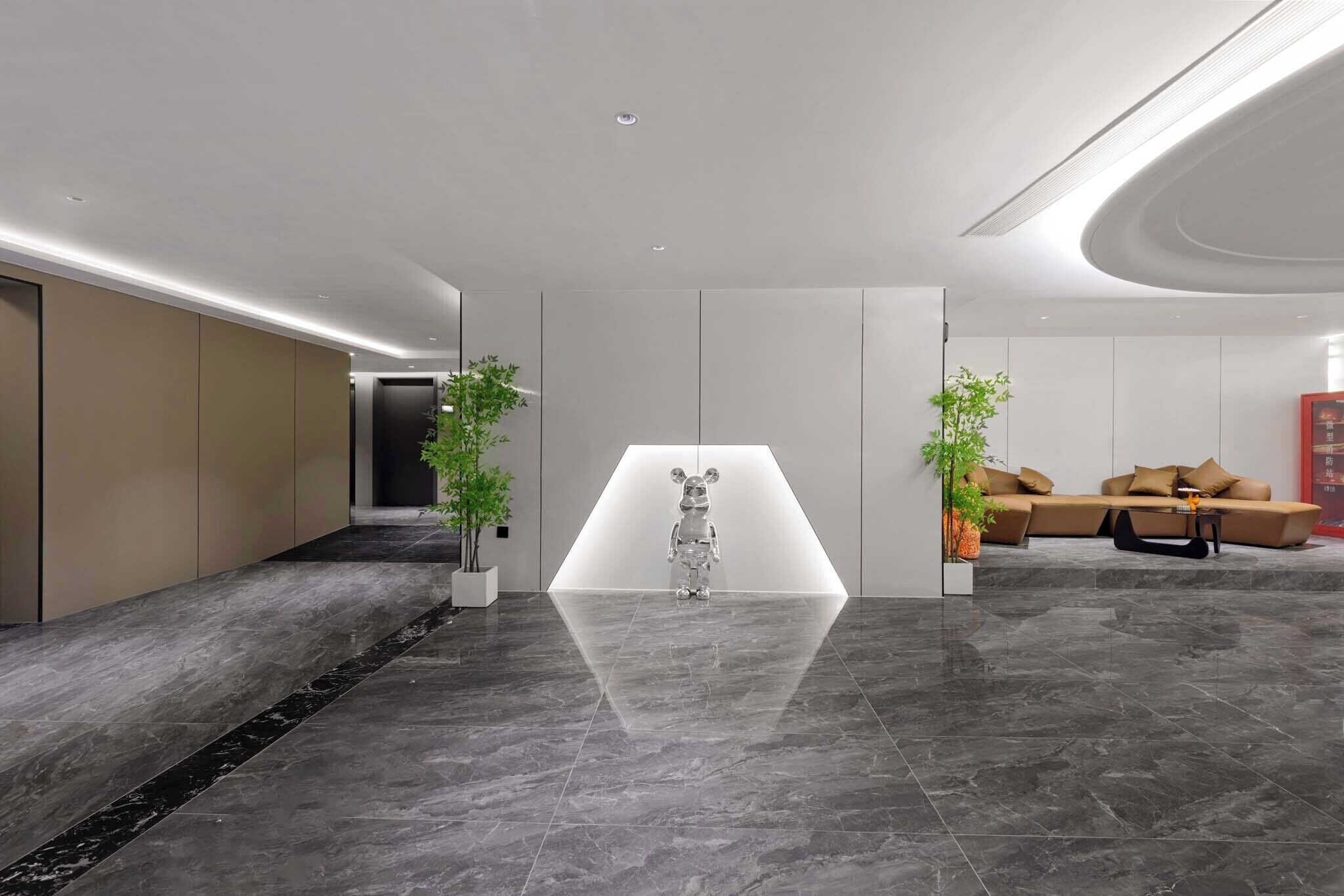 Un vestíbulo moderno con piso reflectante, una escultura central y una zona de estar con sofá y mesa de centro.