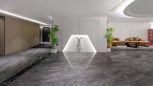 Un vestíbulo moderno con piso reflectante, una escultura central y una zona de estar con sofá y mesa de centro.