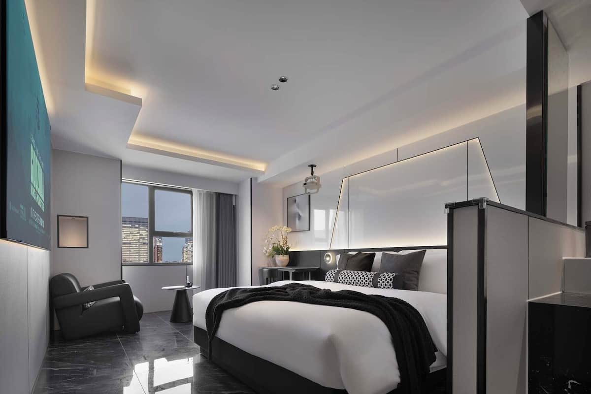 Une chambre d’hôtel moderne dotée d’un grand lit, d’un coin salon, d’un bureau et offrant une vue sur la ville.