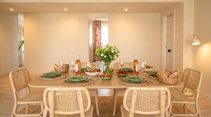 Ein Esszimmer mit einem langen Tisch, Korbstühlen und einer Blumenvase.