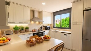 Una cucina moderna con mobili bianchi, una cappa in acciaio inossidabile, una finestra vista verde e un'area pranzo con pane e frutta.
