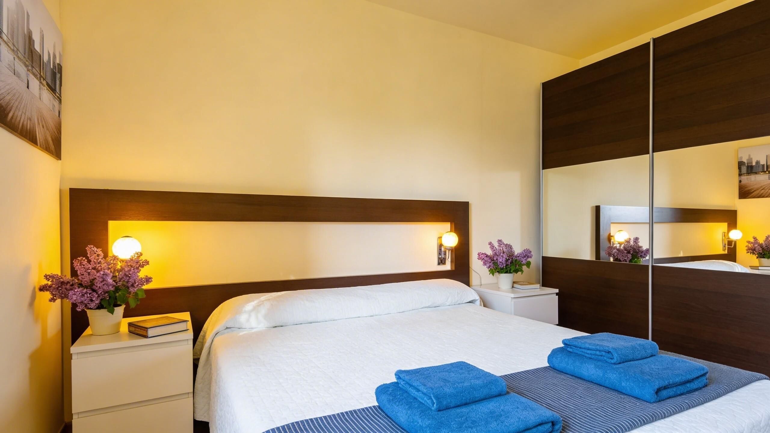 Hotelkamer met een groot bed, nachtkastjes, een spiegel en een stadsgezichtschilderij aan de muur.