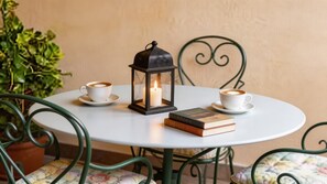 Ein runder Tisch mit zwei weißen Kaffeetassen, einer brennenden Kerze in einer Laterne und einem Stapel Bücher.
