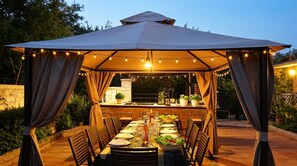 Een overdekt eethoekje met een tafel, stoelen en sfeerverlichting.