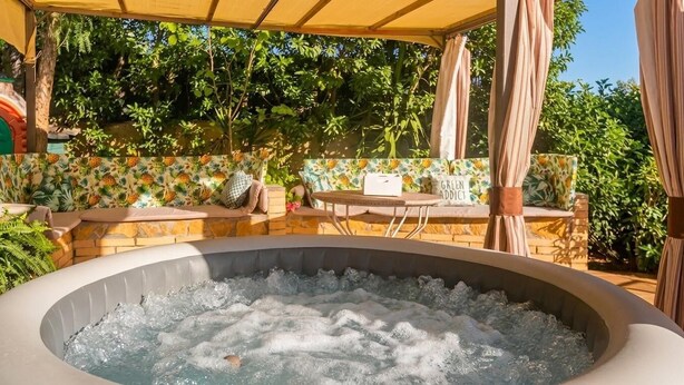 A hot tub with a stone surround, outdoor seating, and a covered area with a view of greenery. - 15 minutes by car / Sitges – Villa Ilus XXL Pool, A/C by Weekly Villas 15 P (Sitges)