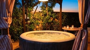 Un bain à remous entouré de verdure, une pergola en bois et une table décorée de bougies.