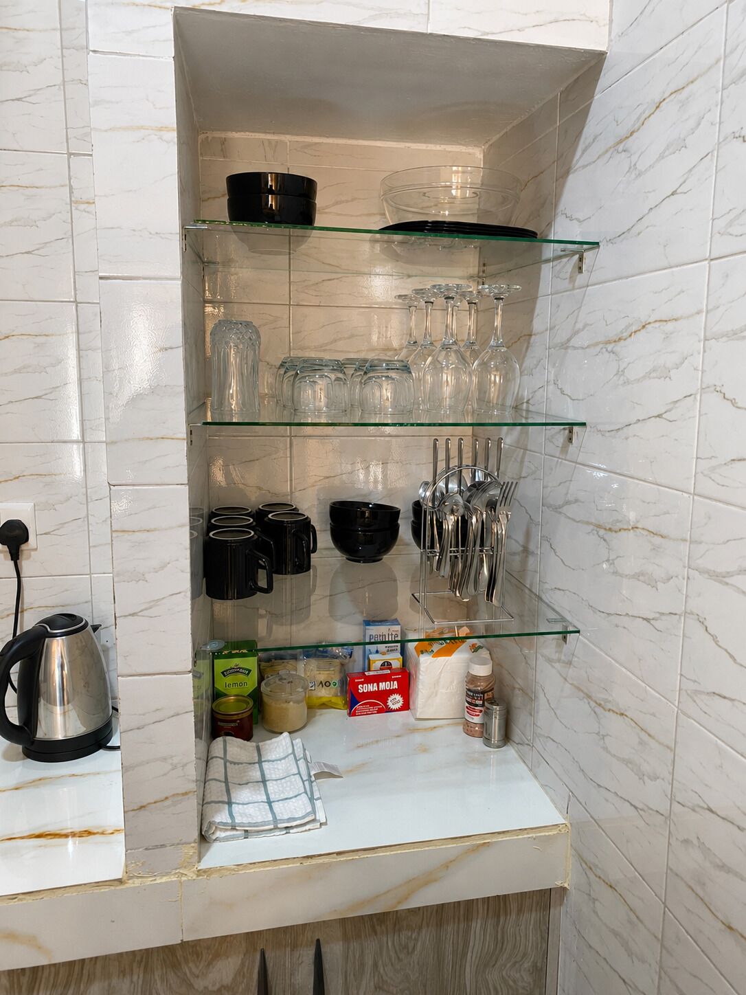 A kitchen with a marble backsplash, a kettle, glassware, and various kitchen utensils.