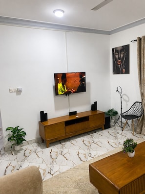 Ein Wohnzimmer mit an der Wand montiertem Fernseher, einer Holz-Unterhaltungsecke, einem schwarzen Sessel und einem Boden mit Marmoroptik.