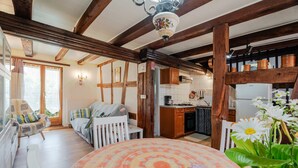 A cozy room with a wooden ceiling, a dining table with a floral tablecloth, a white chair, and a window with curtains. - Gite Le Coquelicot "bi's anstetts" – Authentic Alsatian Farmhouse Retreat (Issenhausen)