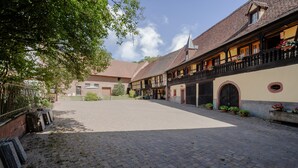 A courtyard with cobblestone pavement, traditional half-timbered buildings, and a clear sky. - Gite Le Coquelicot "bi's anstetts" – Authentic Alsatian Farmhouse Retreat (Issenhausen)