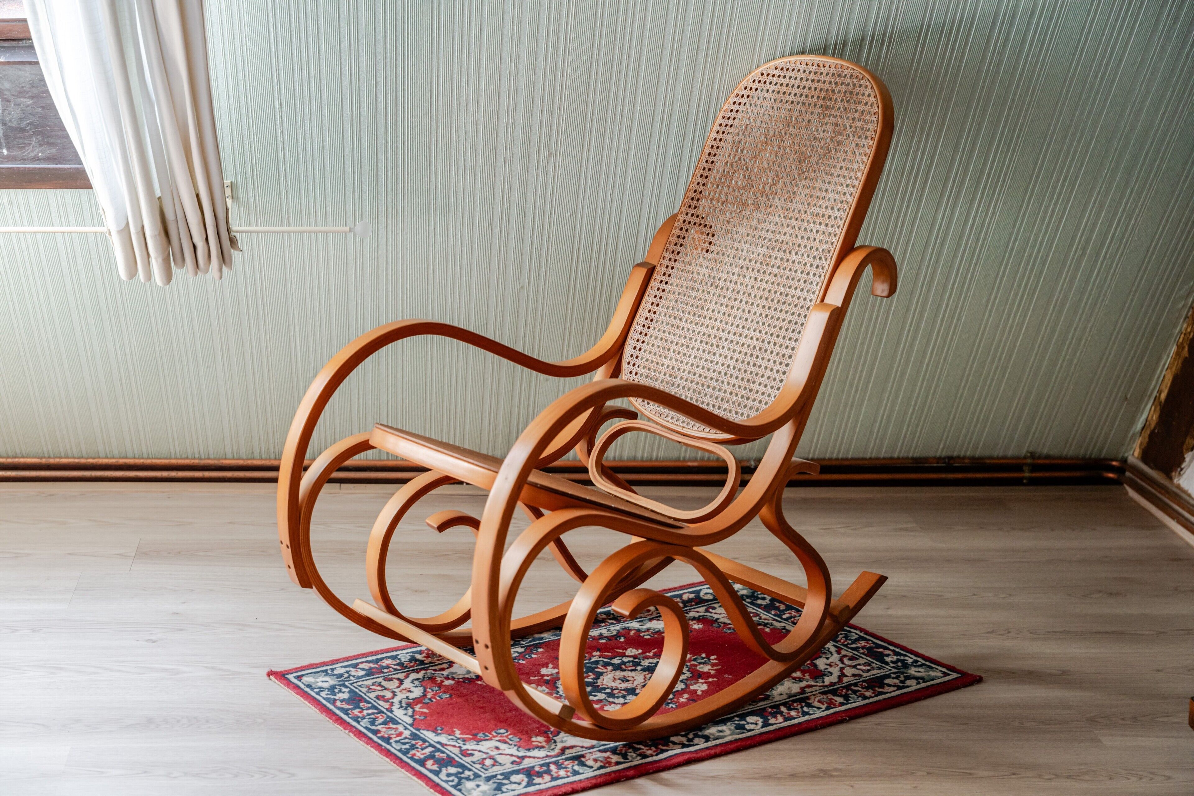 A rocking chair with a woven backrest and wooden frame, positioned on a patterned rug.