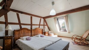 A bedroom with a wooden ceiling, two beds, a nightstand, a chair, and a window. - Gite Le Coquelicot "bi's anstetts" – Authentic Alsatian Farmhouse Retreat (Issenhausen)