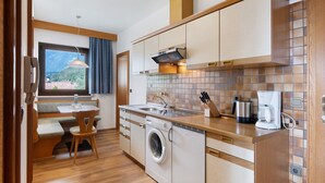 A compact kitchen with a built-in washer, a coffee maker, and a dining area with a bench. - Apartment A4 Spisshof Annex with Panoramic View, Shared Pool and Wi-Fi (Algund)