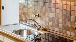 A kitchen with a stainless steel sink, a tiled backsplash, and wooden cabinets. - Apartment A4 Spisshof Annex with Panoramic View, Shared Pool and Wi-Fi (Algund)