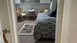 Une chambre à coucher avec un lit, une chaise, une petite table, un radiateur, une fenêtre et une décoration représentant une girafe.