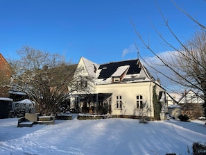 Une maison avec un toit en pente, un porche à l’avant et une cour enneigée.