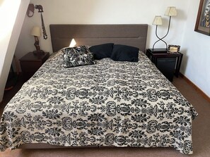 A bed with a patterned bedspread, a headboard, two bedside lamps, a nightstand with a picture frame, and wall art.