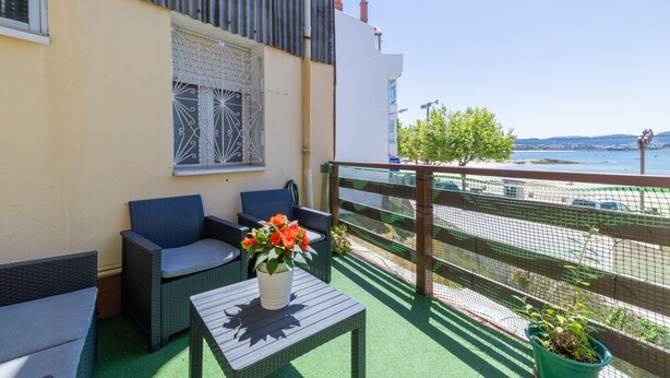 Een balkon met zitplaatsen buiten, een tafel met een bloevas en uitzicht op zee.