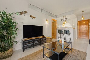 Een moderne woonkamer met een flatscreen televisie, een glazen salontafel en een eethoek met stoelen en een houten deur.