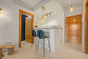 Een moderne keuken met een centraal eiland, twee barkrukken, hanglampen en houten deuren.